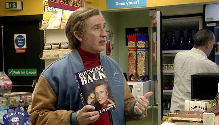 Alan Partridge holding a copy of his book 'Bouncing Back'